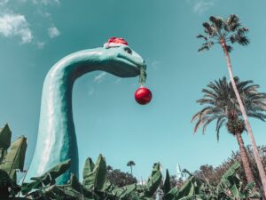dinosaur in a santa hat, holding a bauble in its mouth. Photo by Photo by Alyssa Eakin on Unsplash